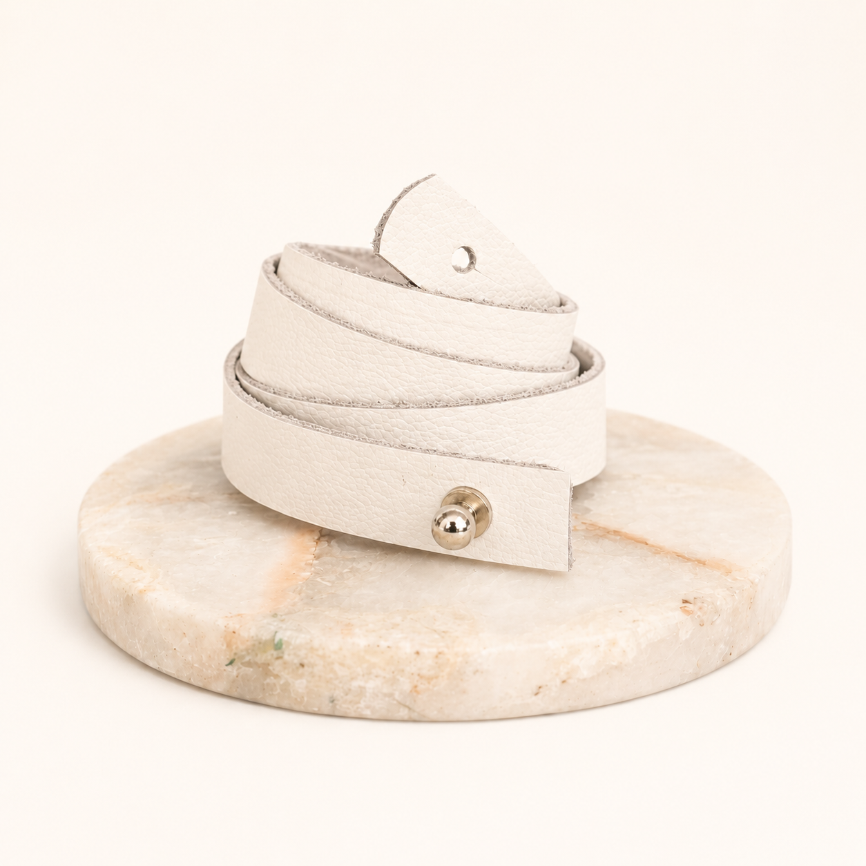 White leather bracelet with a silver clasp on a marble stand against a white background